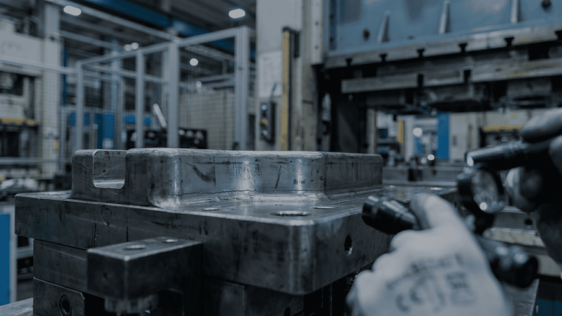 Close-up view of a worn metal stamping die inside a press shop, with visible surface abrasion and operators inspecting the tool, illustrating how die wear leads to quality shifts in stamped parts.