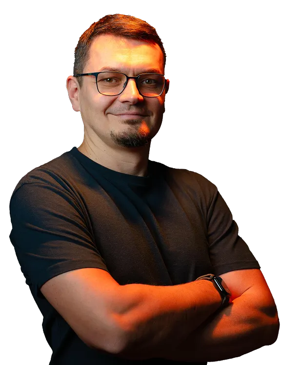 Ein Mann mit kurzen braunen Haaren, einer Brille und einem schwarzen T-Shirt steht mit verschränkten Armen und lächelt in die Kamera.