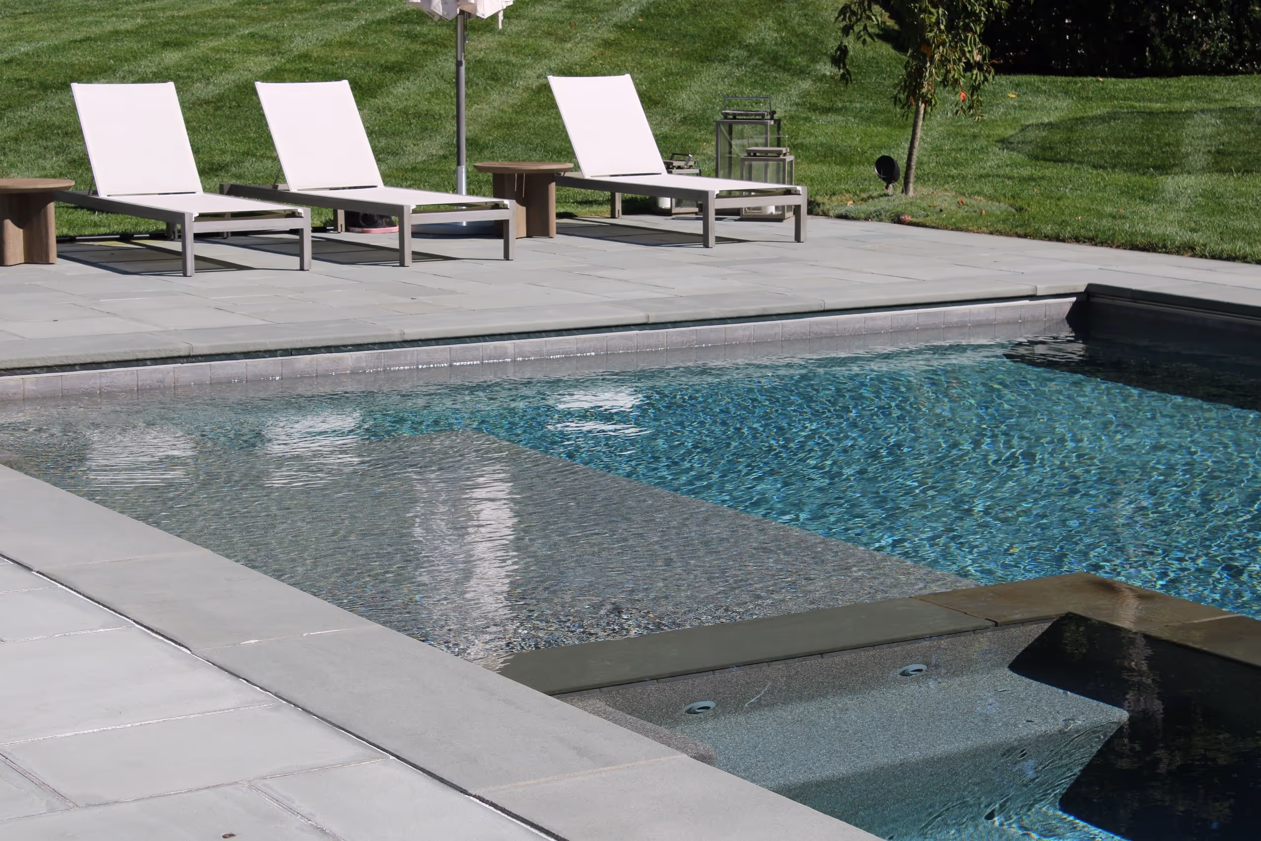 Modern backyard pool with stone patio and lounge chairs in New Canaan, CT by New Canaan Pool Service