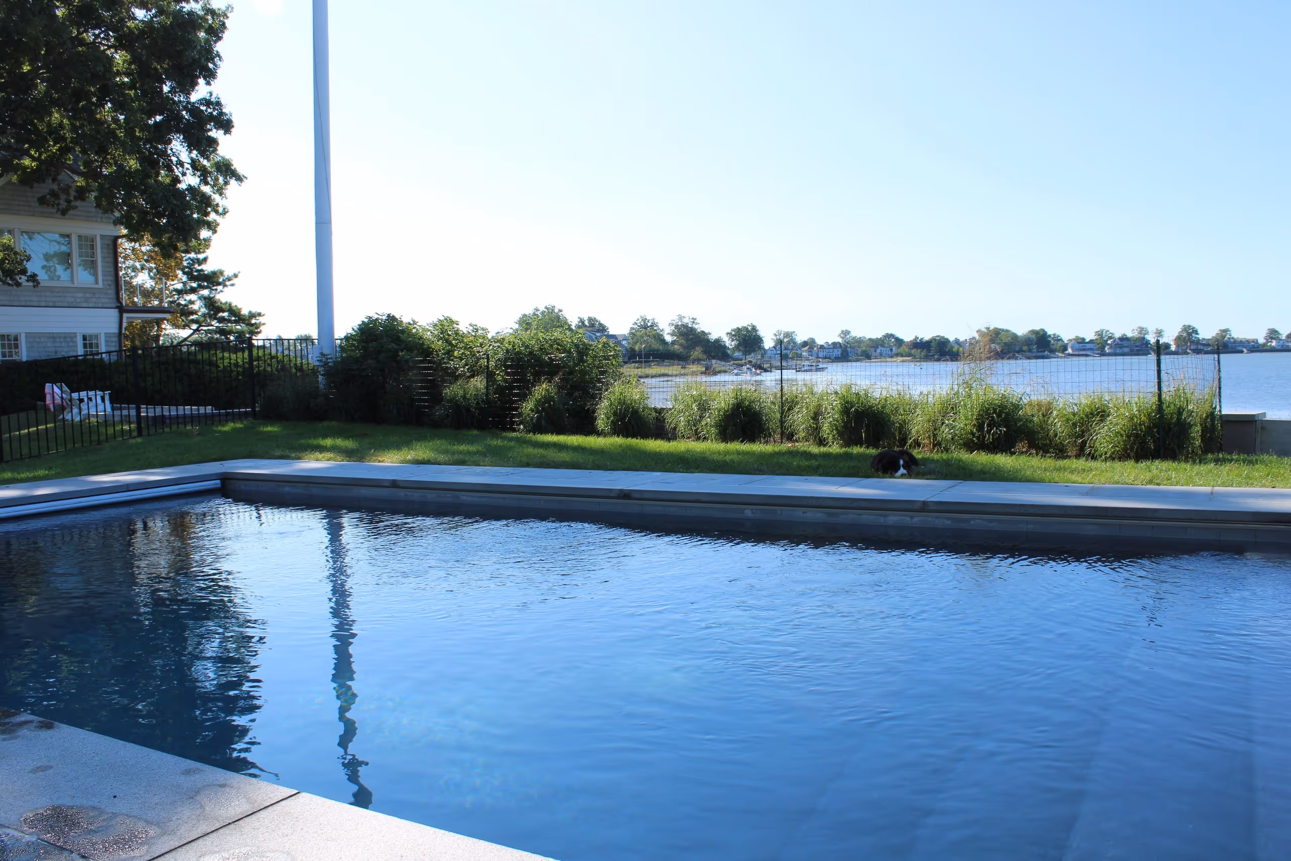 Modern backyard pool with waterfront view and landscaped lawn in New Canaan, CT by New Canaan Pool Service