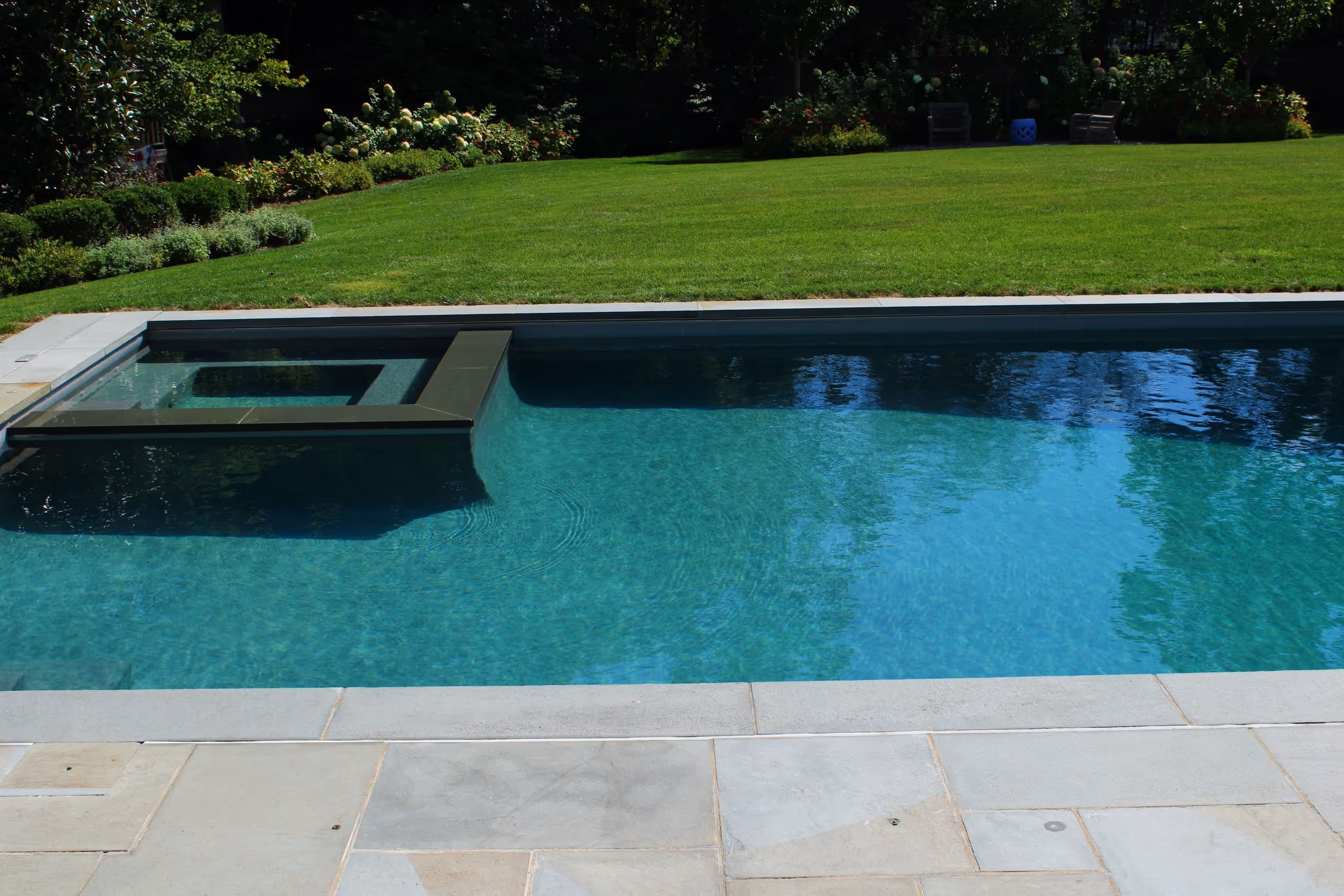 Close-up view of modern pool and raised spa with stone decking and landscaped backyard in Greenwich, CT by New Canaan Pool Service