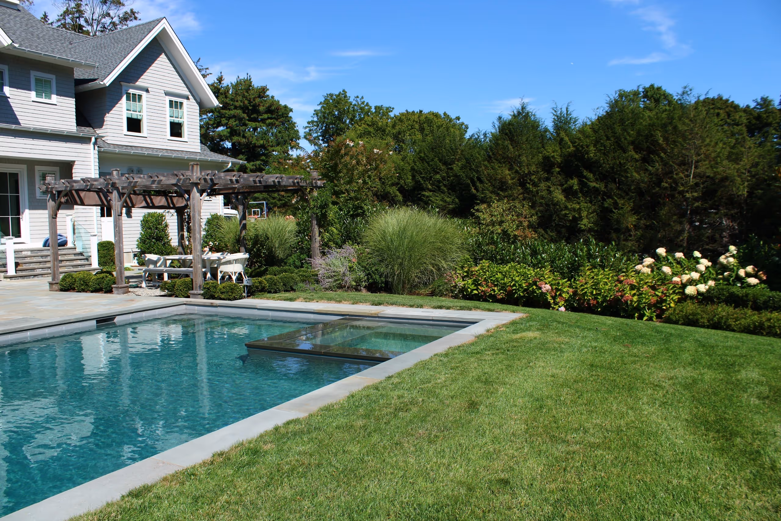 Backyard pool with attached spa and pergola seating area in New Canaan, CT by New Canaan Pool Service