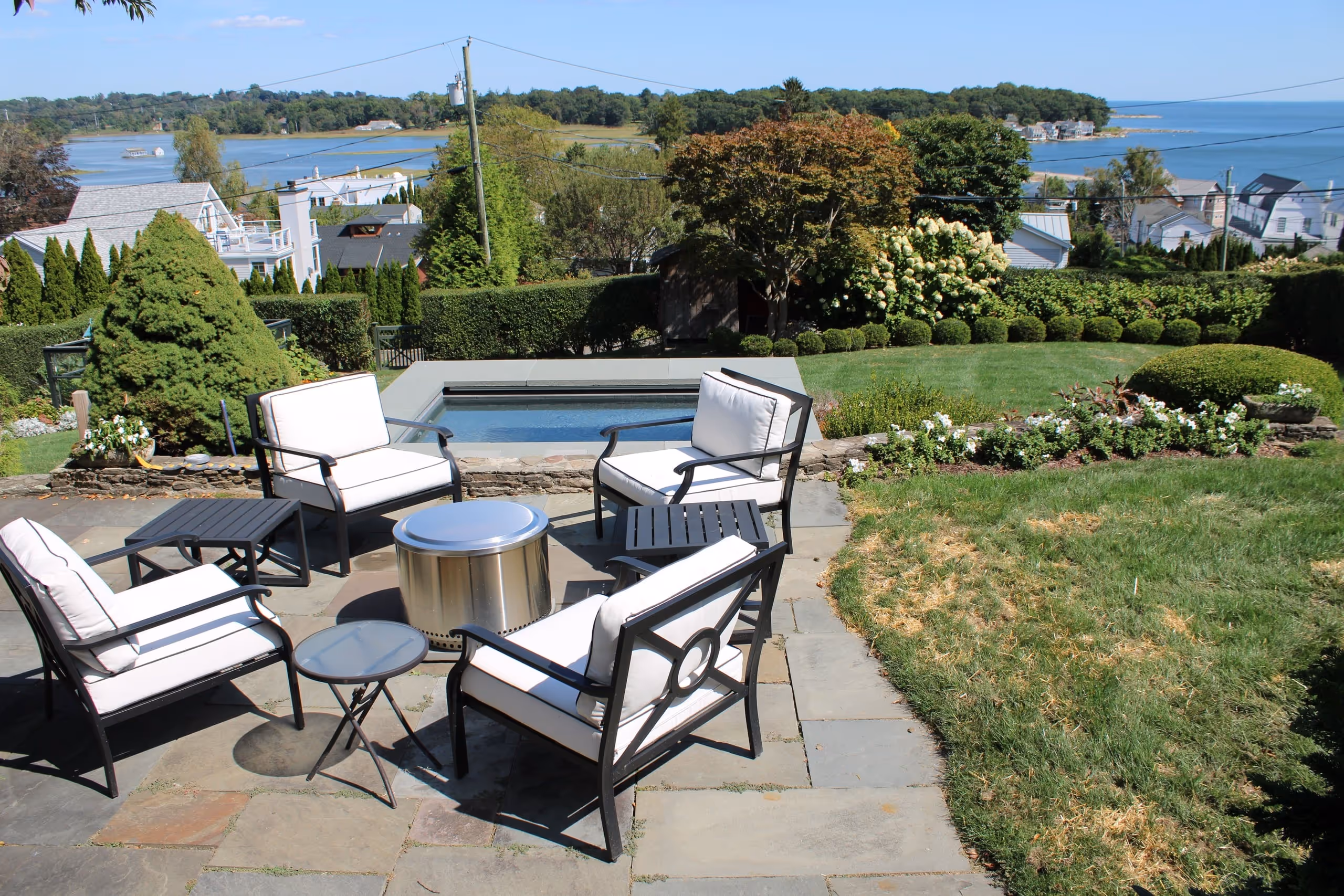 Coastal backyard pool with stone patio, modern seating, and ocean view in Greenwich, CT by New Canaan Pool Service