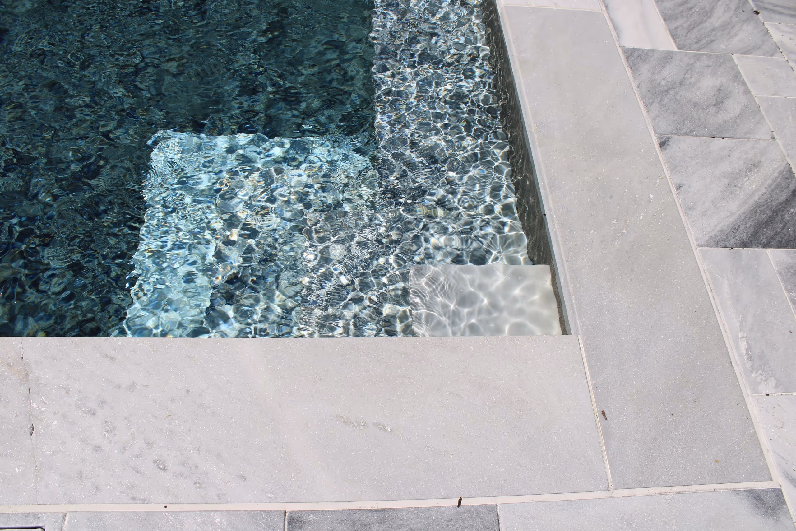 Luxury pool step detail with marble-style stone coping and shimmering clear water in New Canaan, CT by New Canaan Pool Service