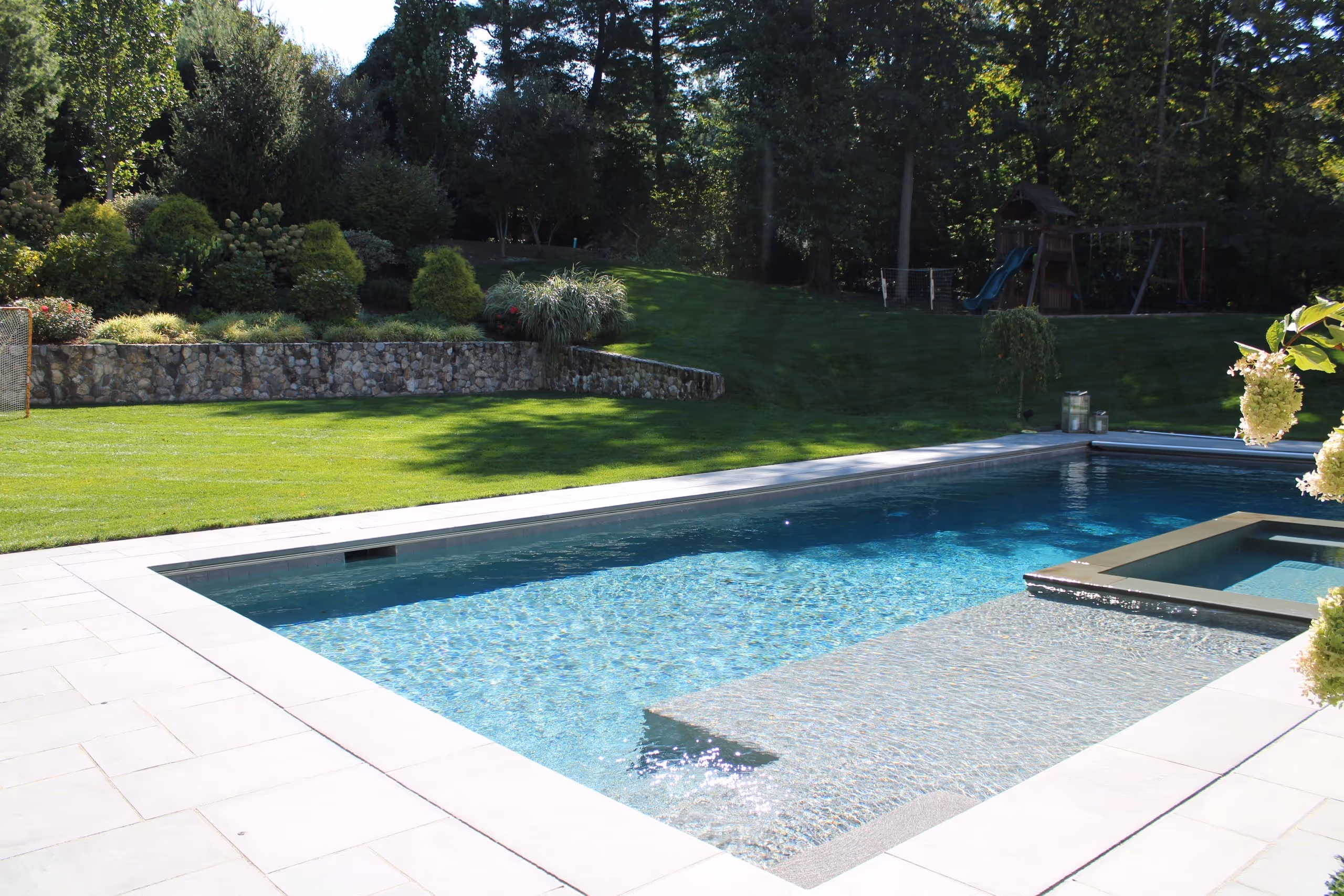 Custom inground pool with spa and stone patio surrounded by greenery in New Canaan, CT by New Canaan Pool Service