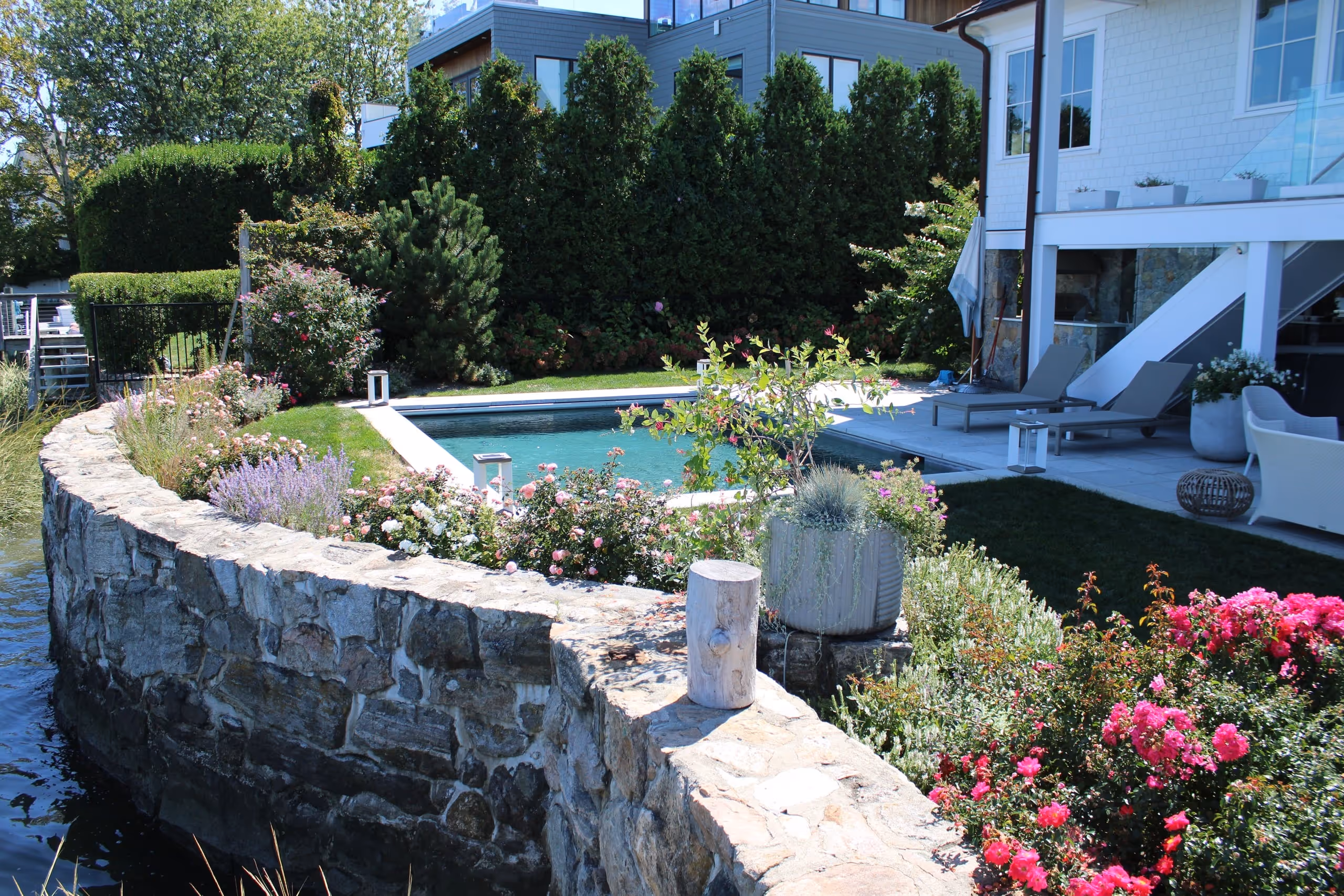 Waterfront backyard with inground pool, stone wall, and colorful garden landscaping overlooking the sound in Darien, CT by New Canaan Pool Service