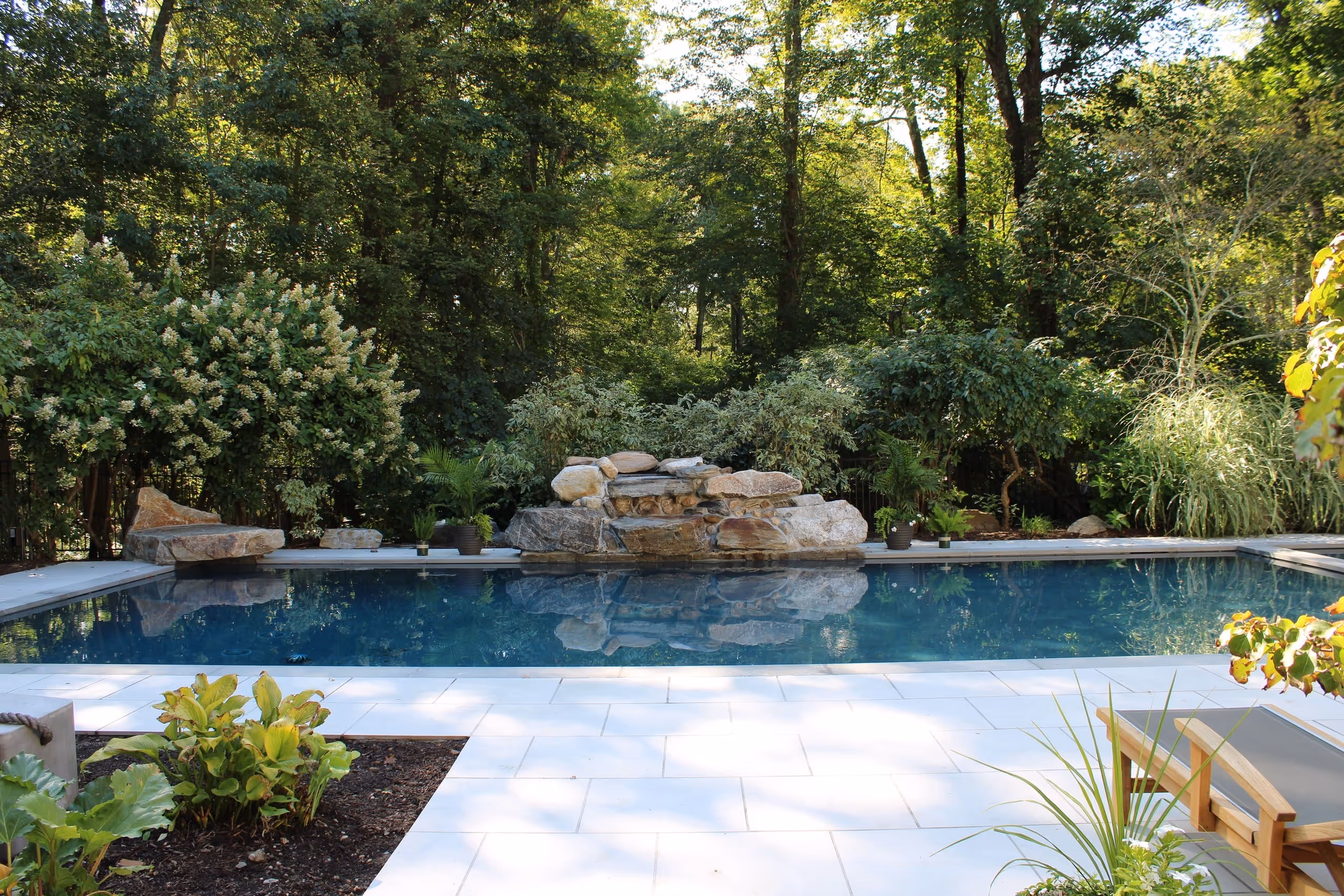 Backyard pool with natural stone waterfall and surrounding garden landscaping in New Canaan, CT by New Canaan Pool Service