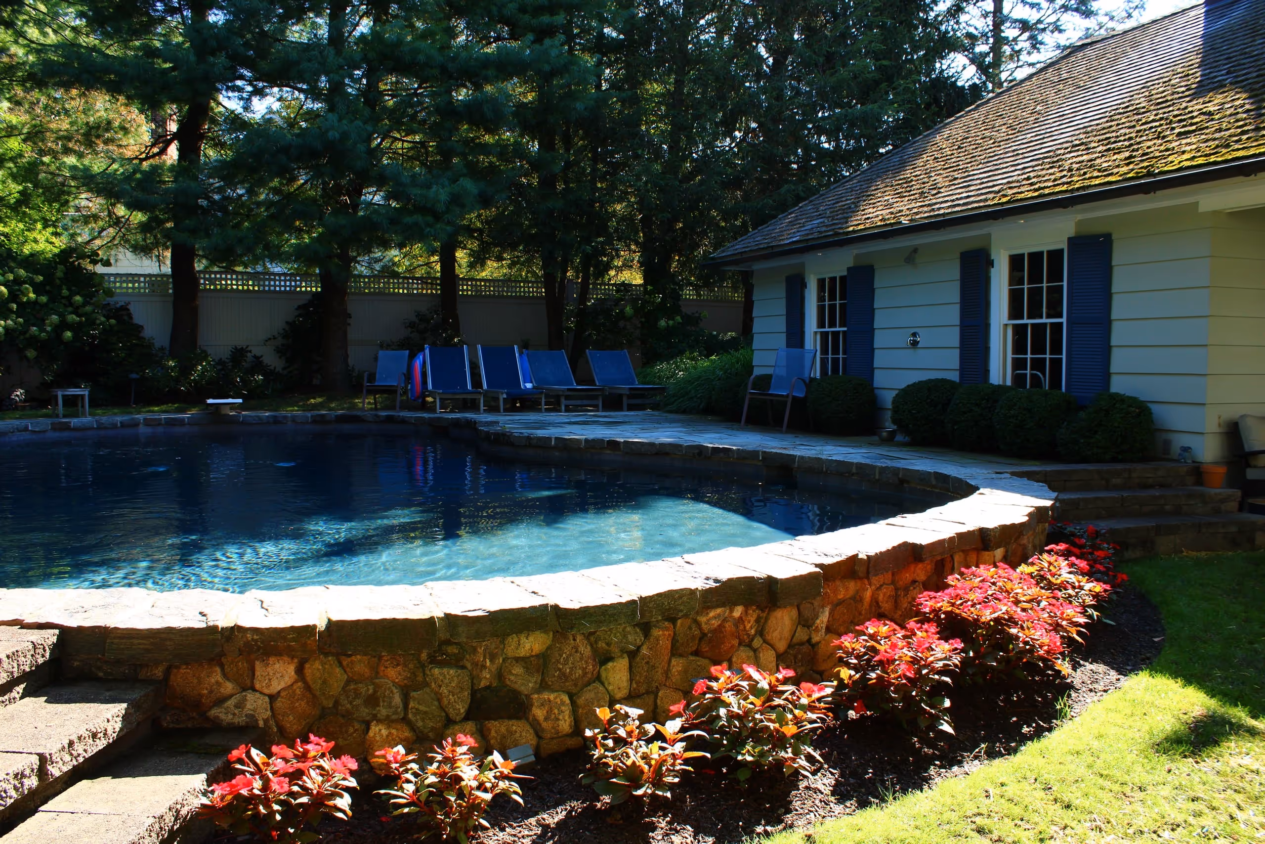 Stone-walled backyard pool with lounge chairs and landscaped garden in New Canaan, CT by New Canaan Pool Service