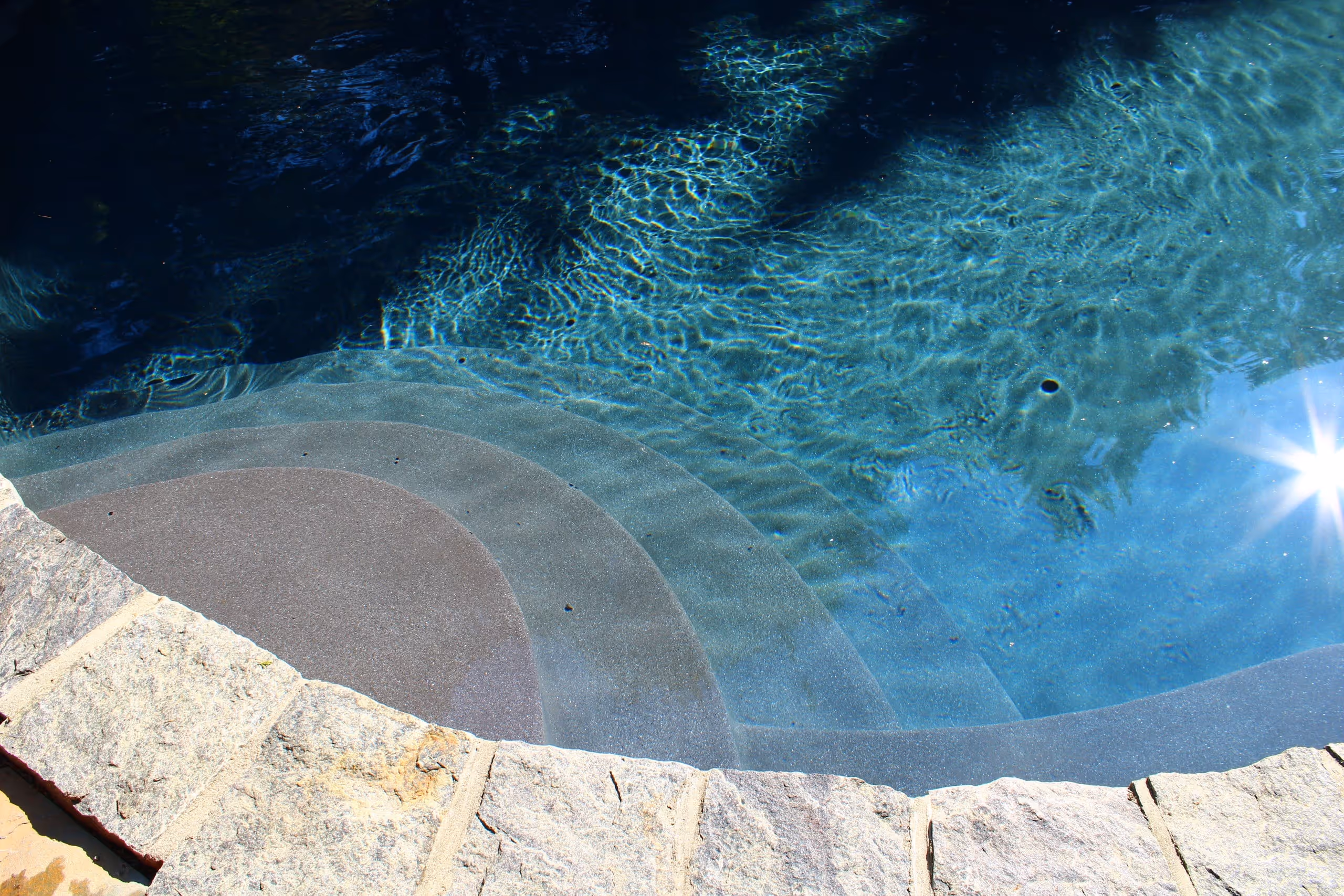 Close-up of stone pool steps with sunlight reflecting on water in New Canaan, CT by New Canaan Pool Service