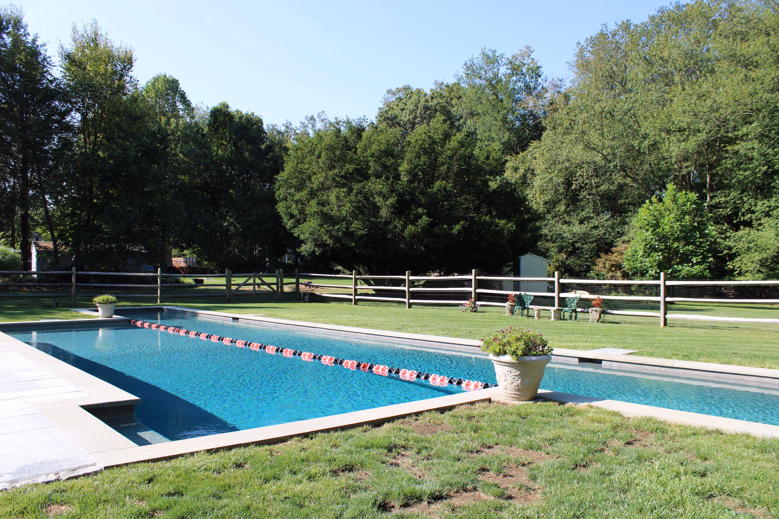 Backyard lap pool with lane divider and landscaped yard in New Canaan, CT by New Canaan Pool Service