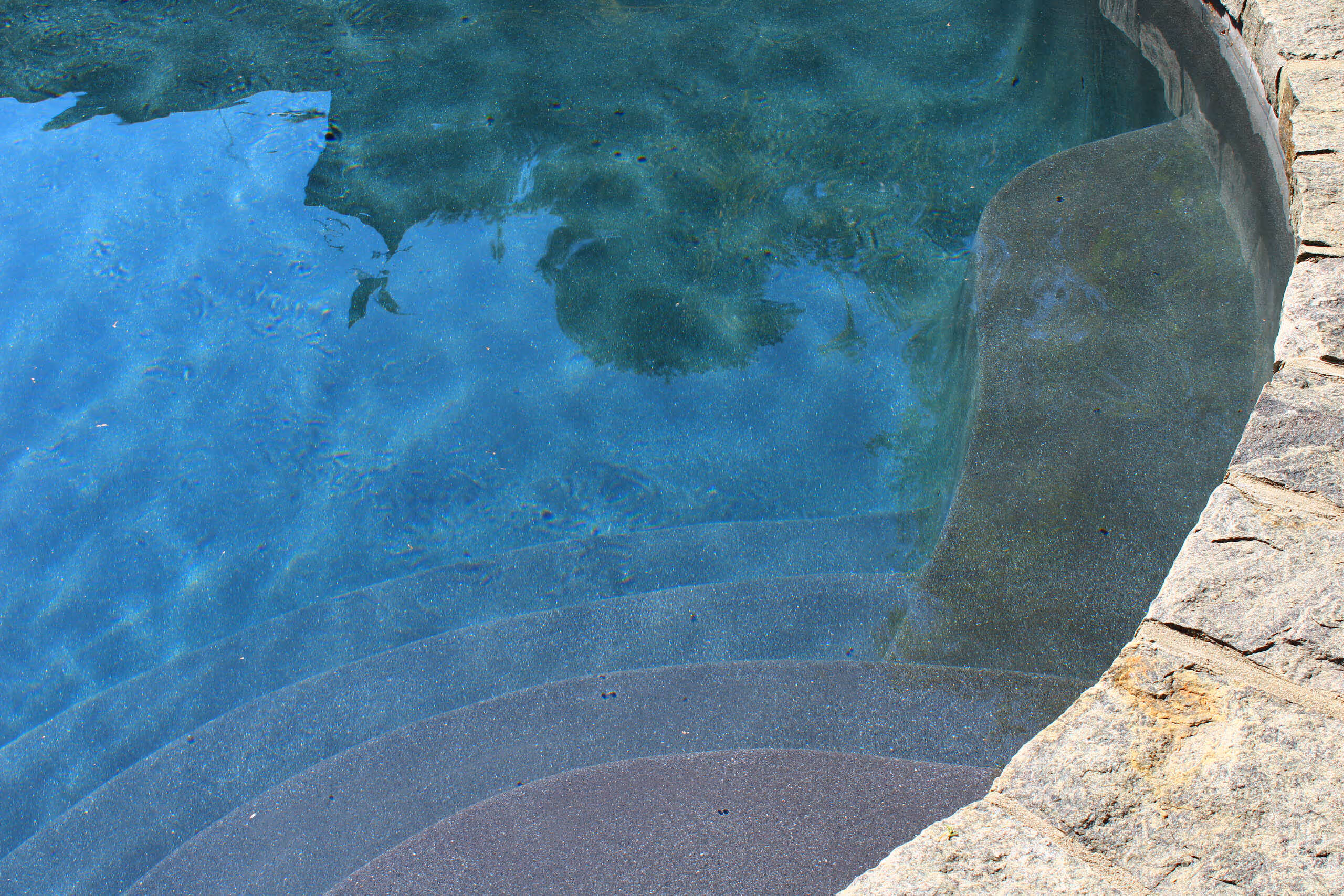 Close-up of curved stone pool steps with clear blue water in New Canaan, CT by New Canaan Pool Service