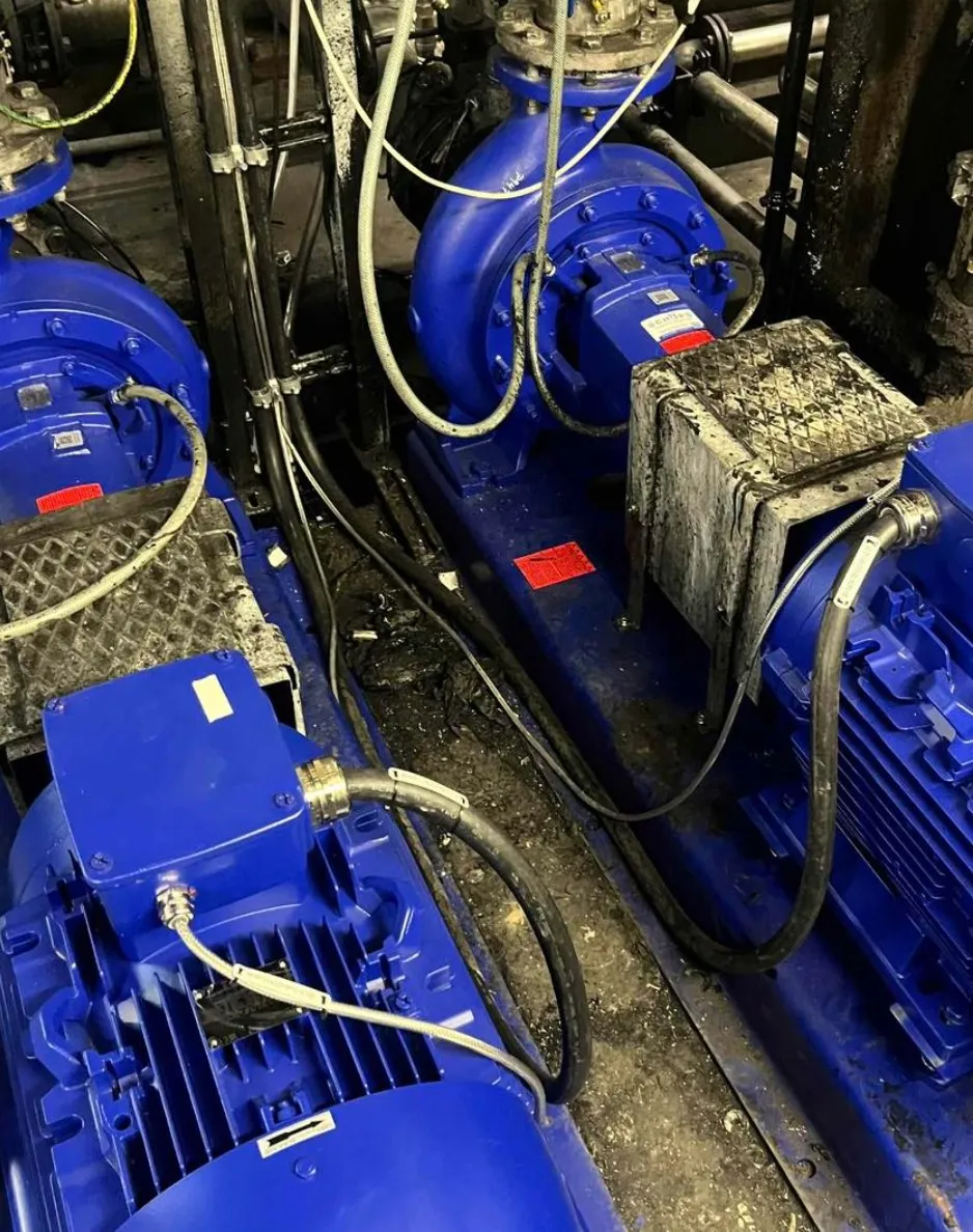 Close-up of blue industrial electric motors and piping with visible cables on a dirty floor.