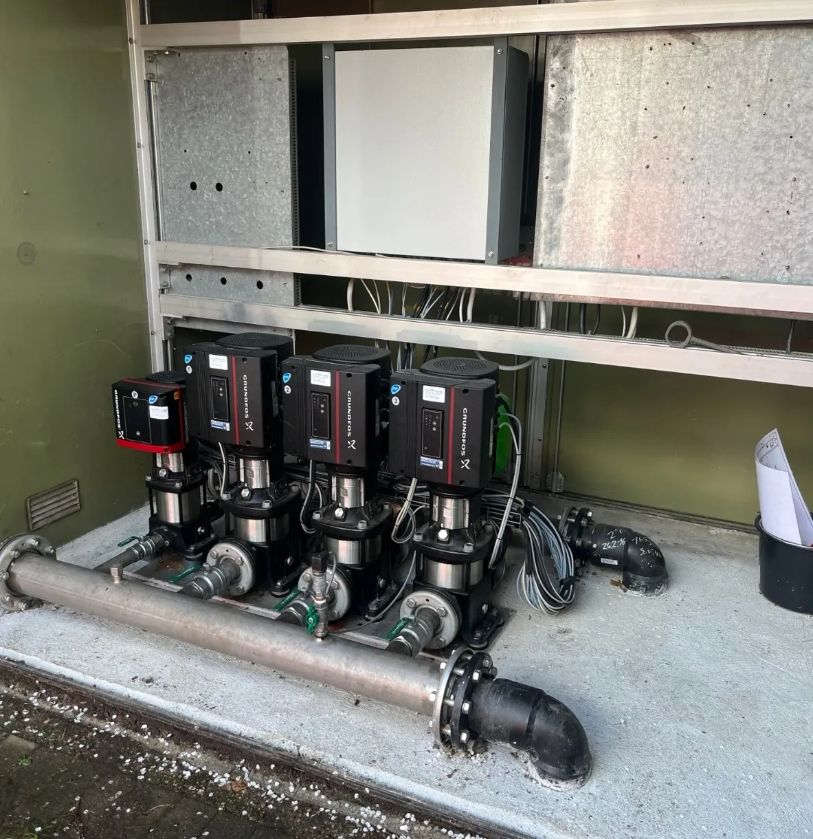 Four industrial Grundfos pumps installed on a concrete platform with connected piping and wiring.