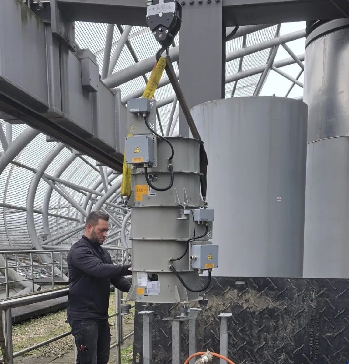 Man working on a suspended large industrial cylindrical component inside a metal structure.