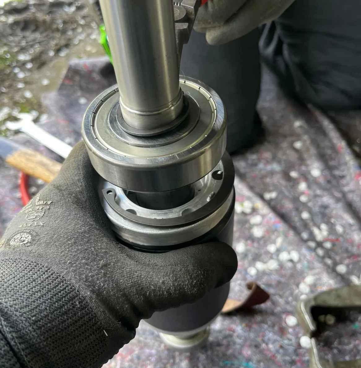 Gloved hands holding and repairing a metal bearing on a cylindrical mechanical part.