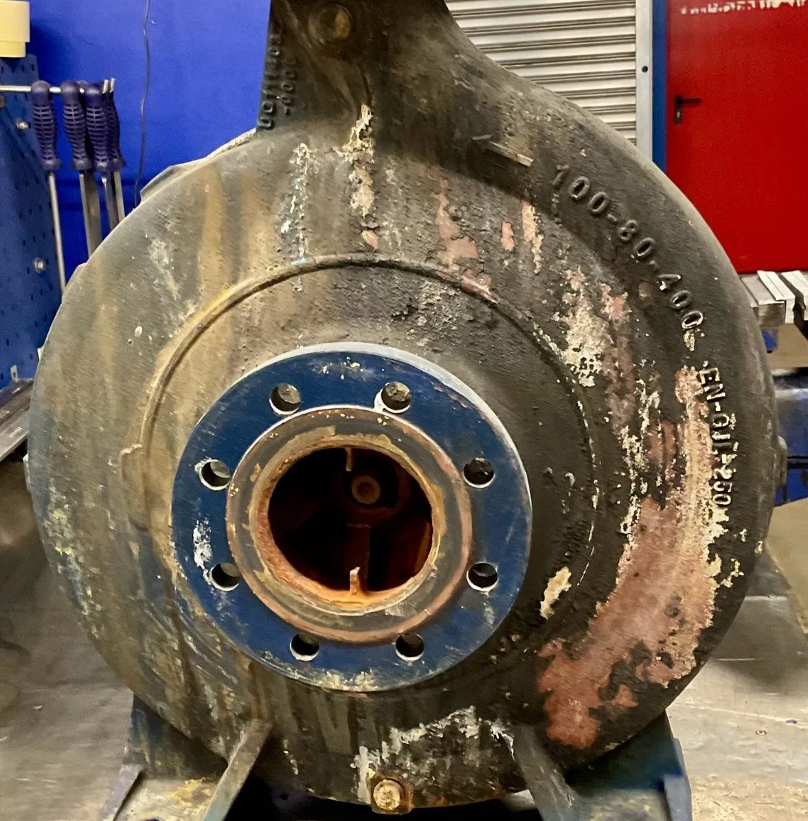 Close-up of a worn industrial metal component with a blue flange and rusted internal parts in a workshop setting.