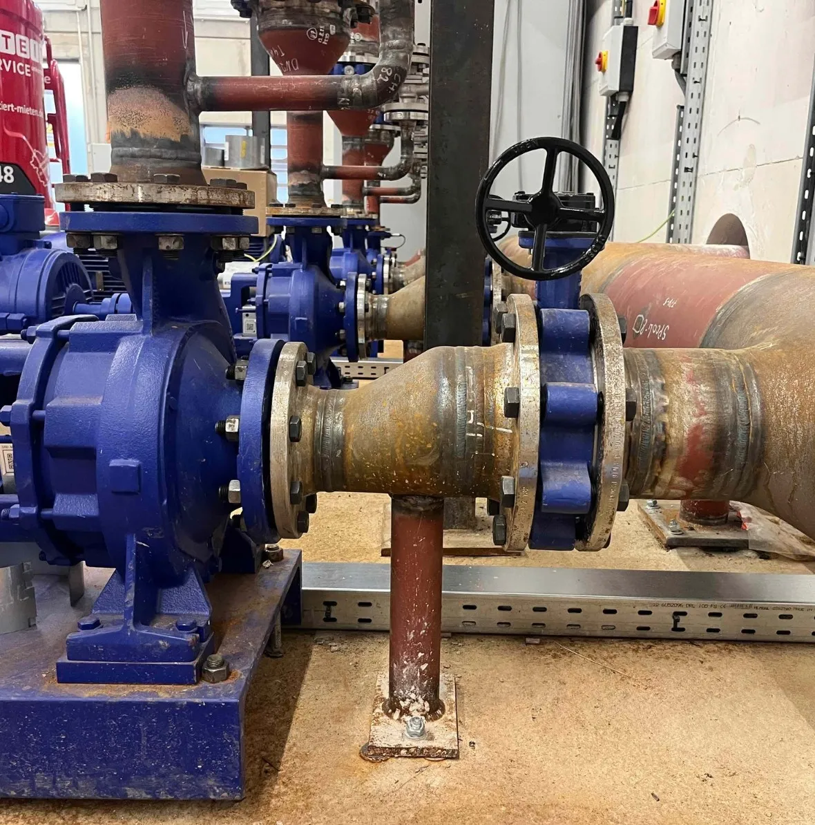 Industrial blue water pumps connected to rusty metal pipes with valves in a utility room.