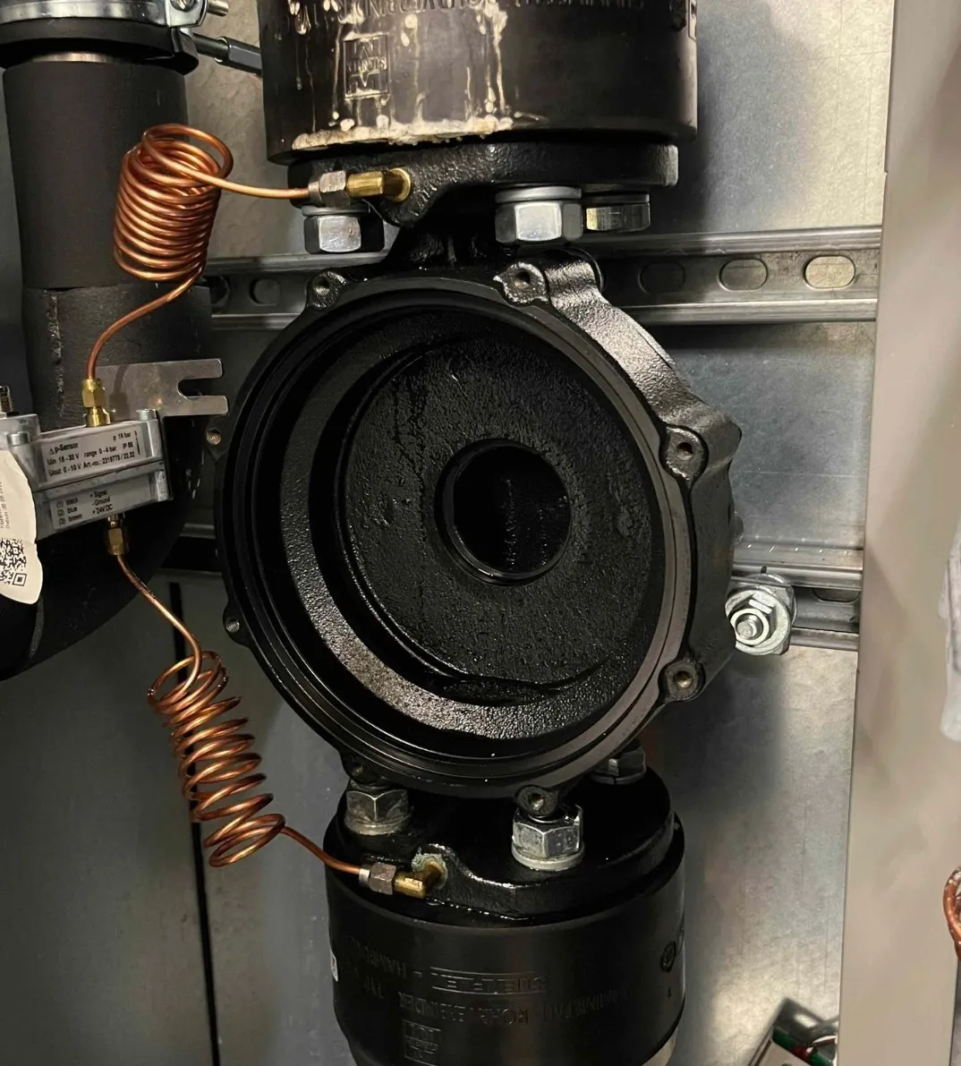 Close-up of industrial black valve or pump with coiled copper tubes and mounted on a metal surface.