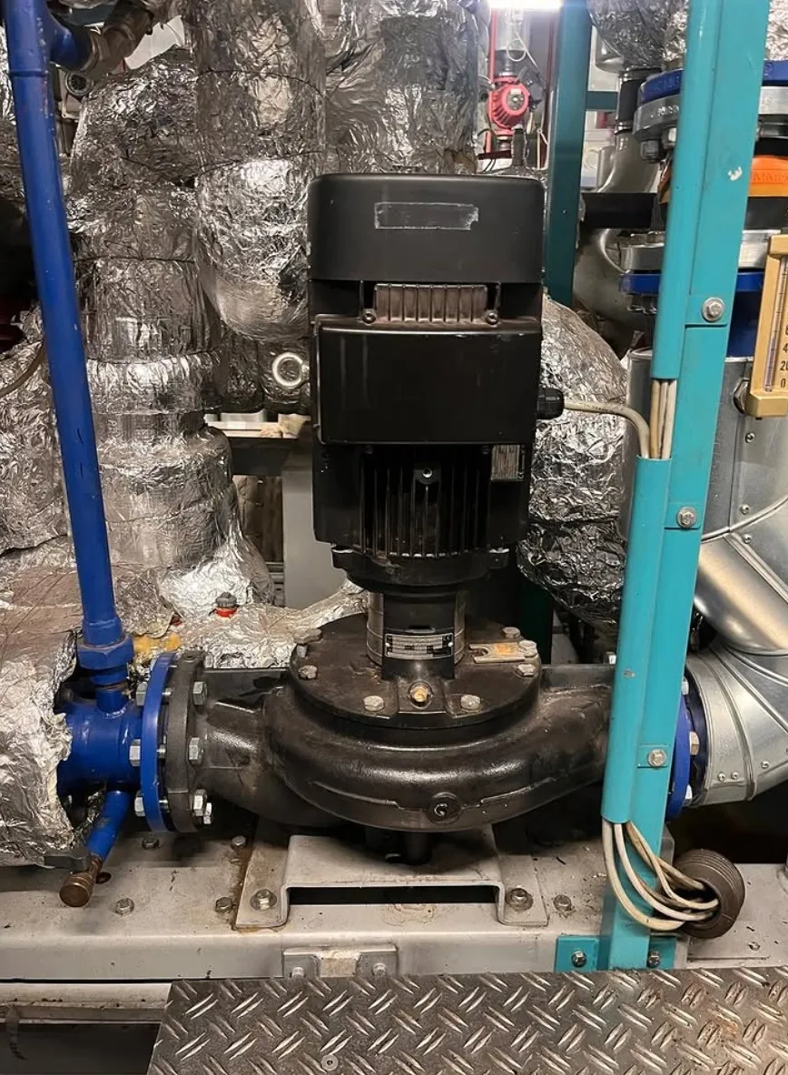 Industrial black motor pump connected to blue pipes with insulated ducting in the background.