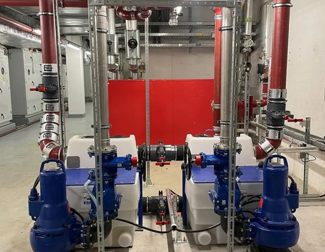 Two blue industrial pumps connected to white tanks with red and silver piping in a mechanical room.