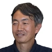 Middle-aged Asian man with short black and gray hair smiling slightly, wearing a dark shirt.