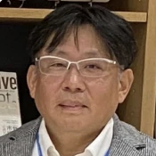 Portrait of a middle-aged man wearing glasses and a light-colored jacket in front of a bookshelf.
