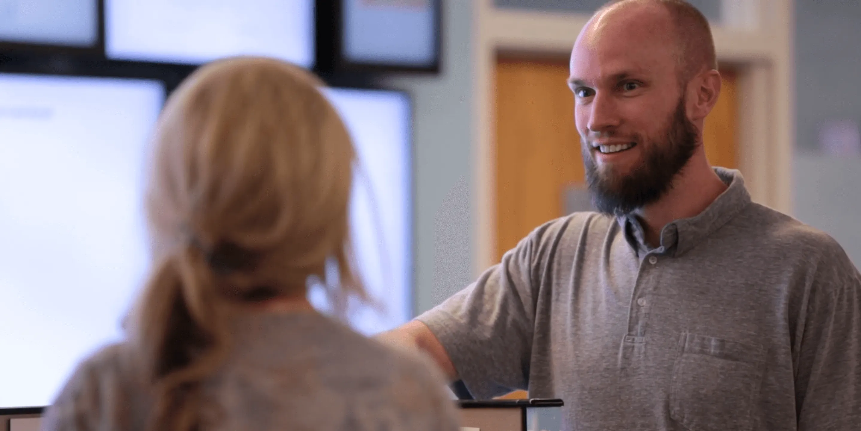 Bearded man smiling and shaking hands with a woman in a grey shirt indoors.