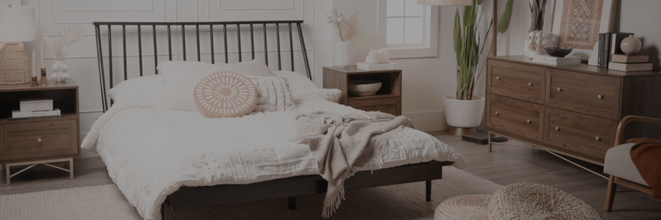 Modern bedroom with a black metal bed frame, white bedding, wooden nightstands, a dresser, plants, and neutral decor.