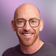 Smiling bald man with glasses and a trimmed beard wearing a gray shirt on a purple gradient background.