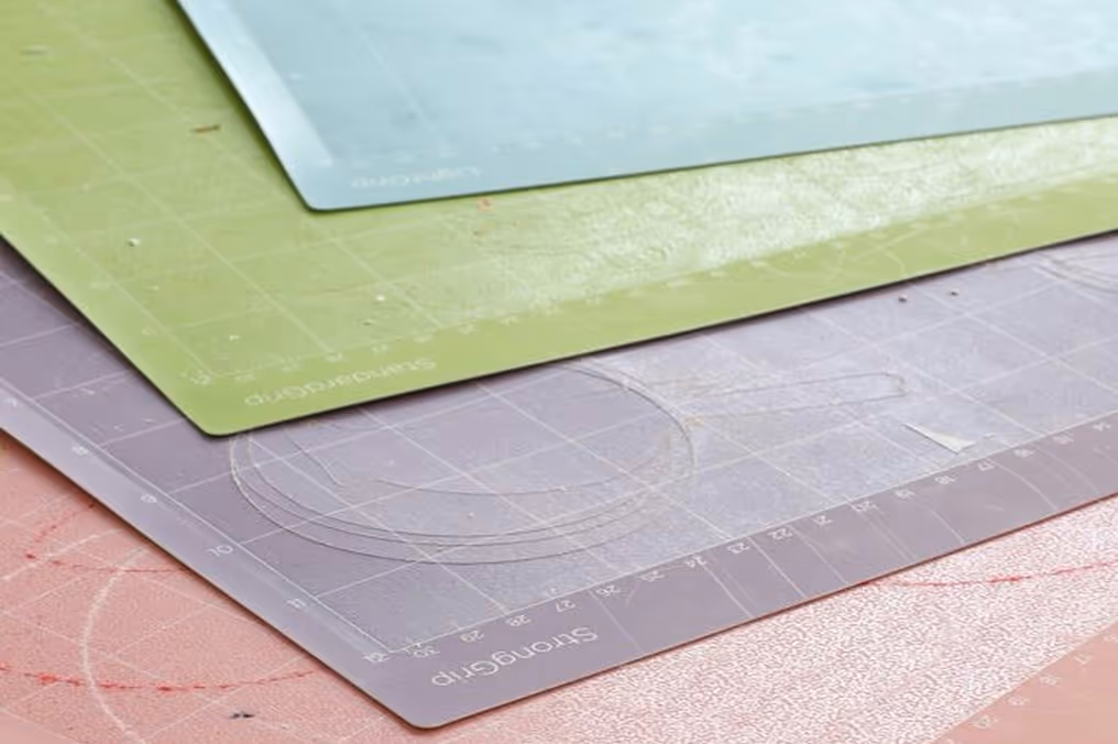 Stack of colorful cutting mats in blue, green, gray, and pink with grid lines and measuring marks.