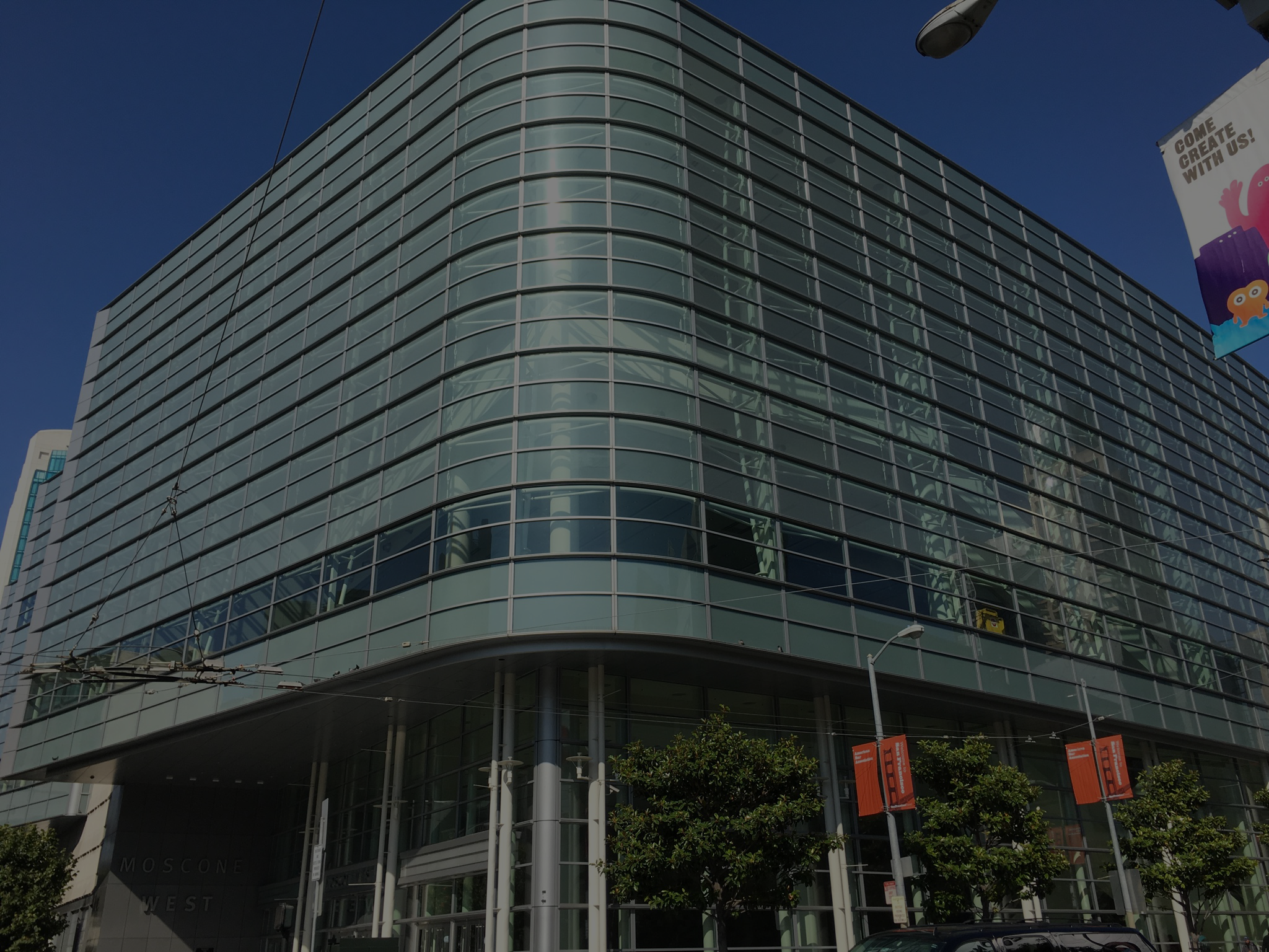 Modern glass building with curved corner and metal framing under deep blue sky, showing Moscone West signage.