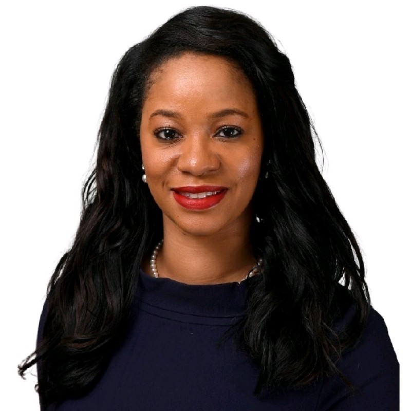 Smiling woman with long black hair, wearing pearl earrings, necklace, and dark top against white background.