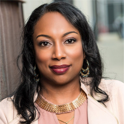 Portrait of a woman with dark hair wearing gold hoop earrings and a textured gold necklace.