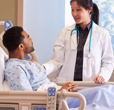 Doctor with stethoscope talking to male patient resting in hospital bed.