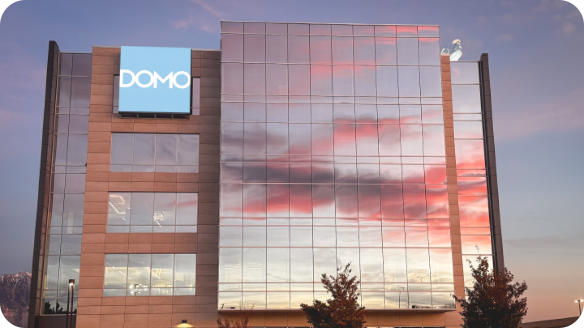 Office building with DOMO sign reflecting a colorful sunset with pink and purple clouds.