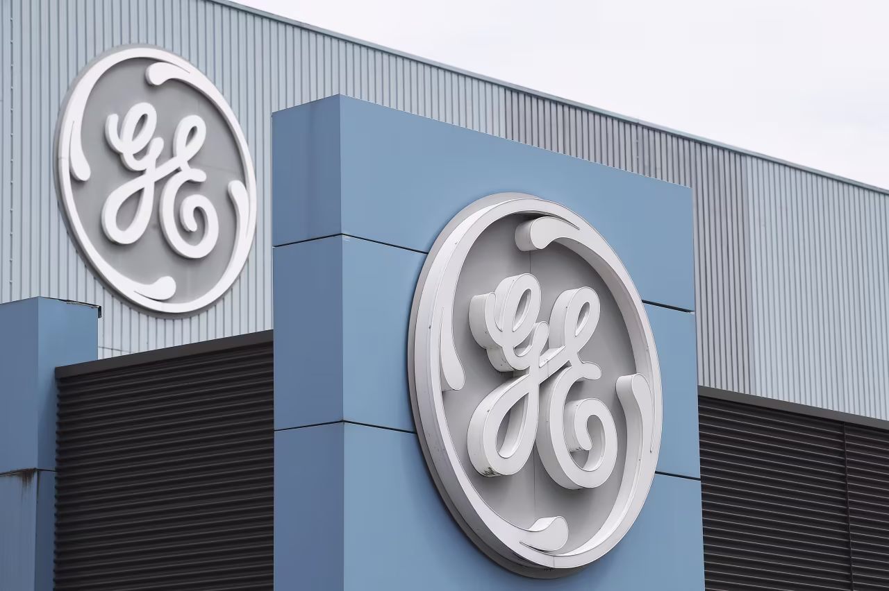 GE logo displayed on a blue building facade with corrugated metal siding and a black vent section.