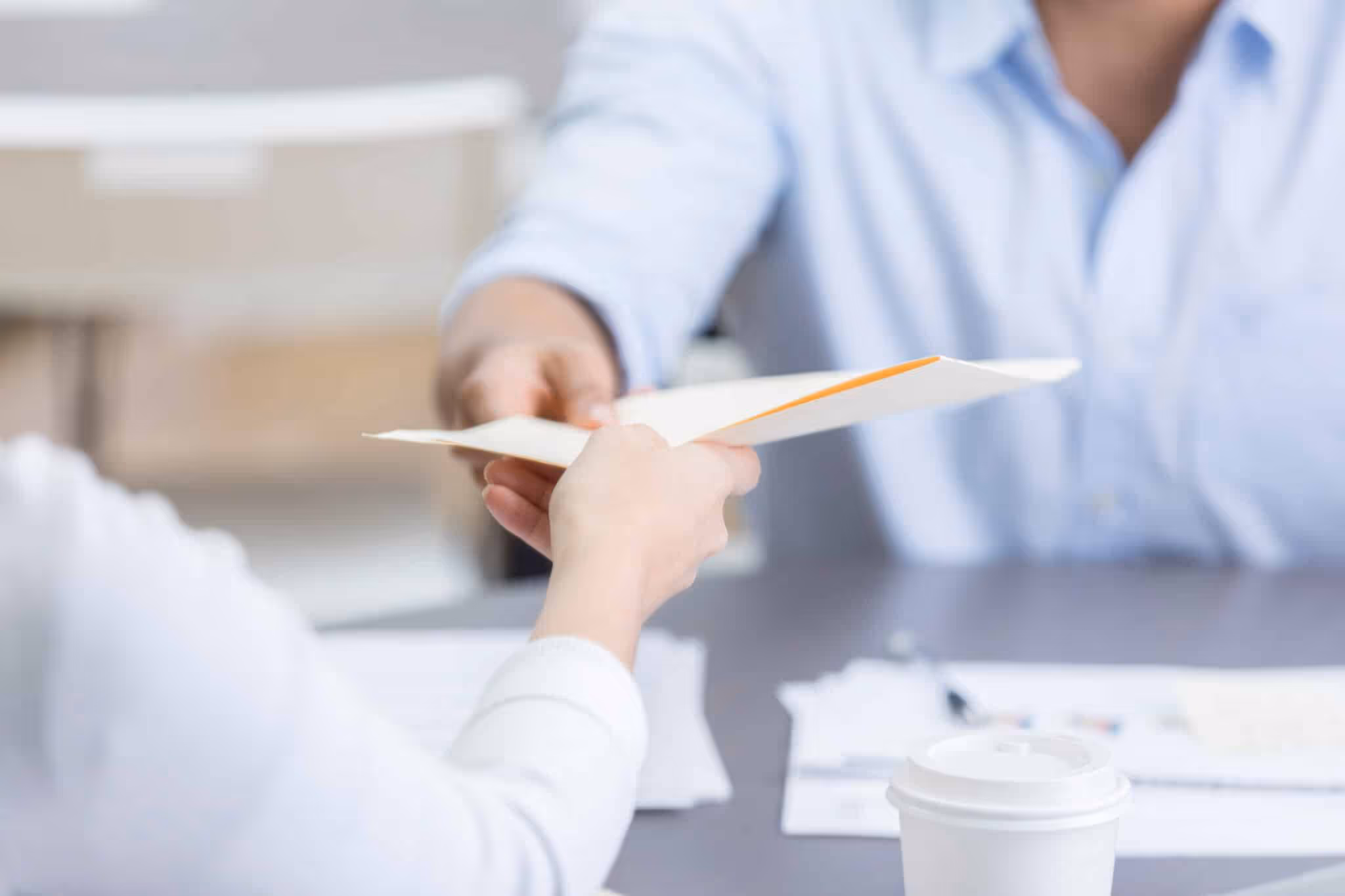 Closeup of two coworkers passing folder across table