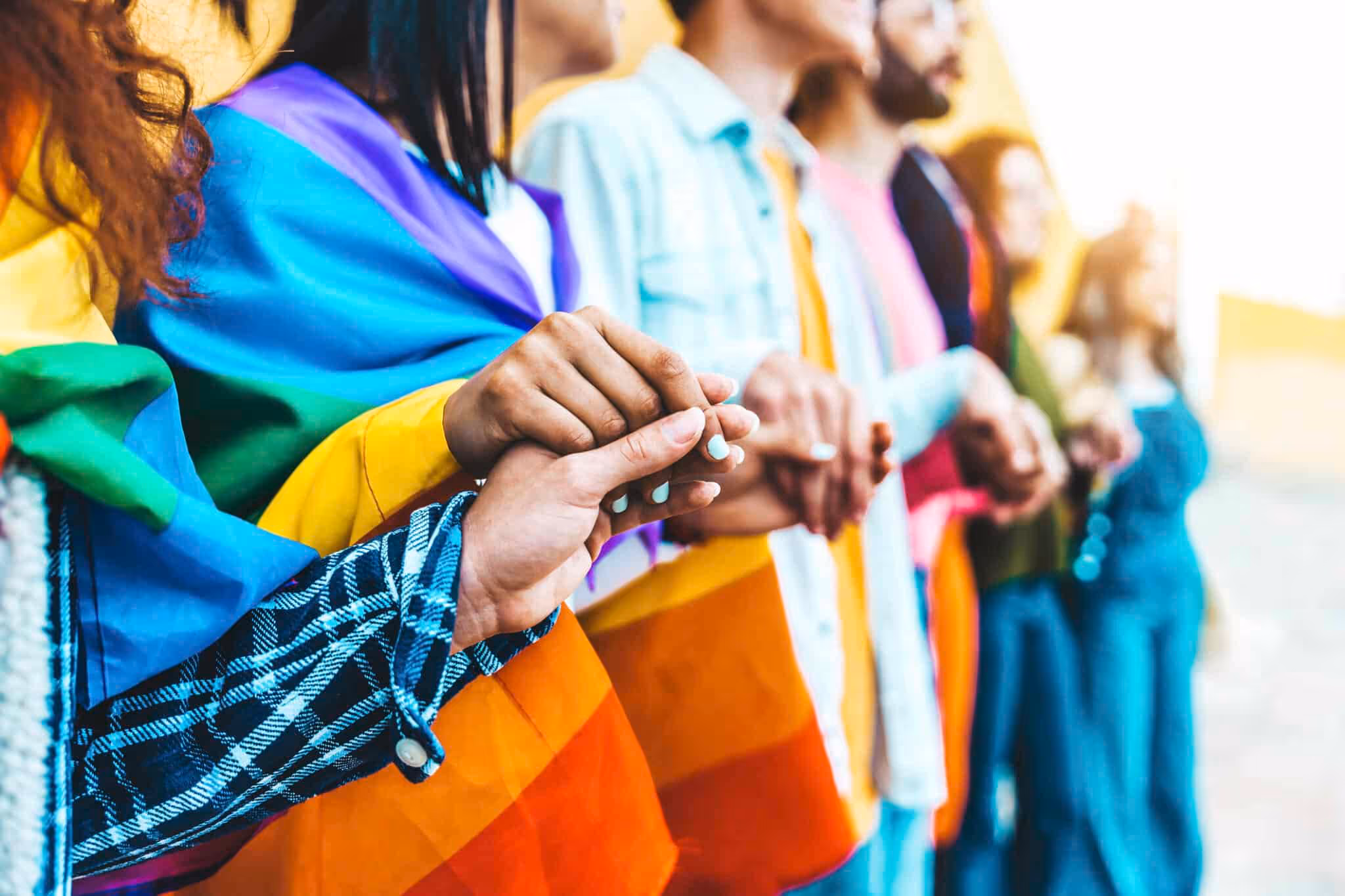 Group of lgbt people holding hands outside - Diverse happy friends hugging outdoors - Gay pride concept with crowd of guys and girls standing together on city street