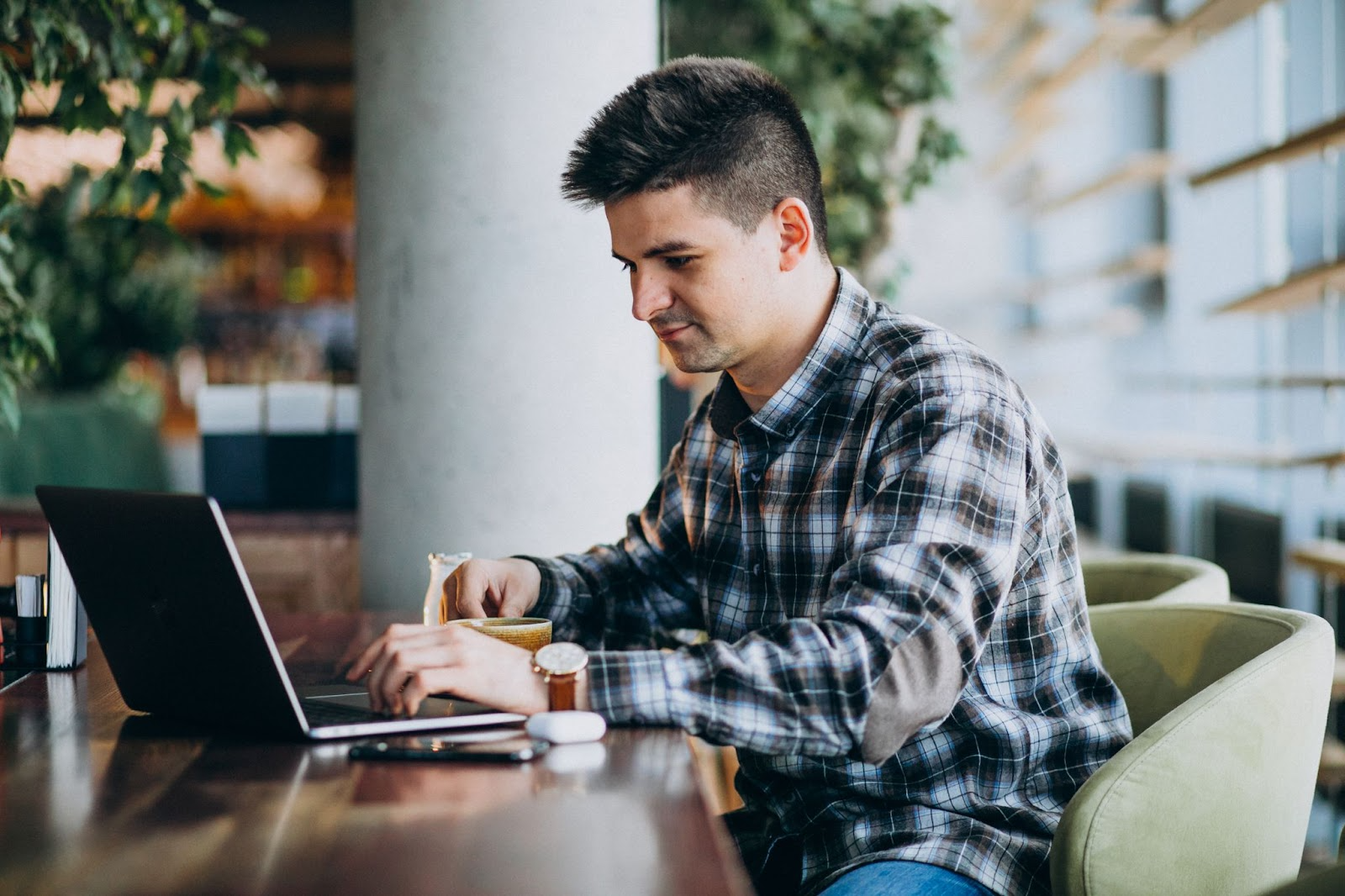 Young man focused on his laptop at a café, symbolizing structure, routine, and personal responsibility developed in a 30-day treatment program