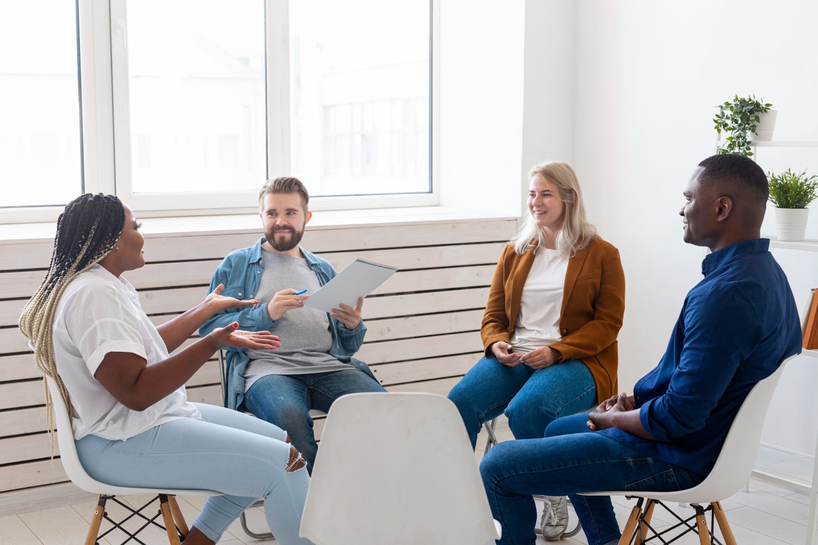 A group of four people in a white room sitting on chairs and participating in a discussion