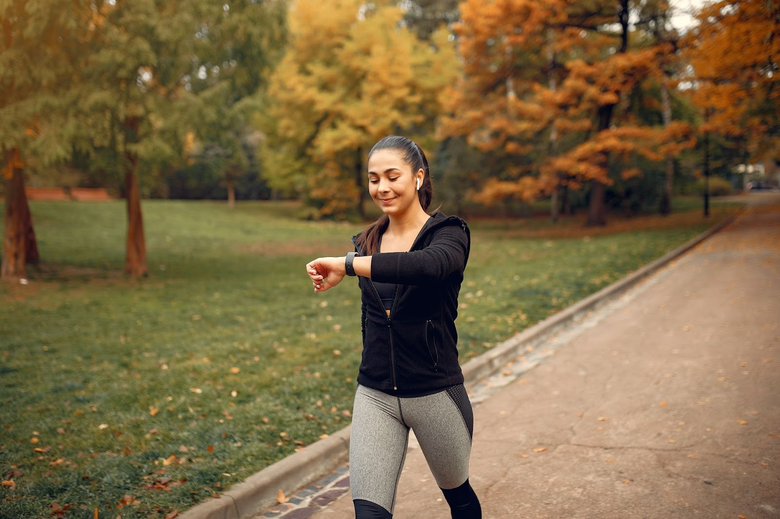 A fit and healthy woman wearing sporty attire looking at a smartwatch while walking in a park