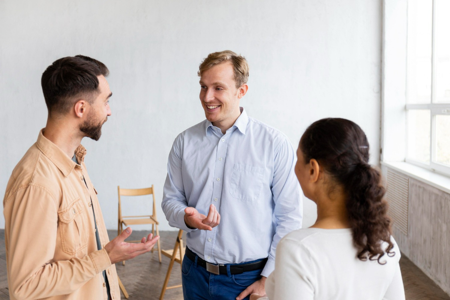 Two men and one woman standing and facing each other while talking in a counseling room