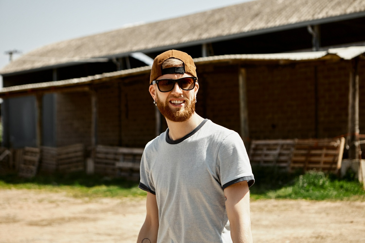 A man outside a warehouse wearing shades and a cap