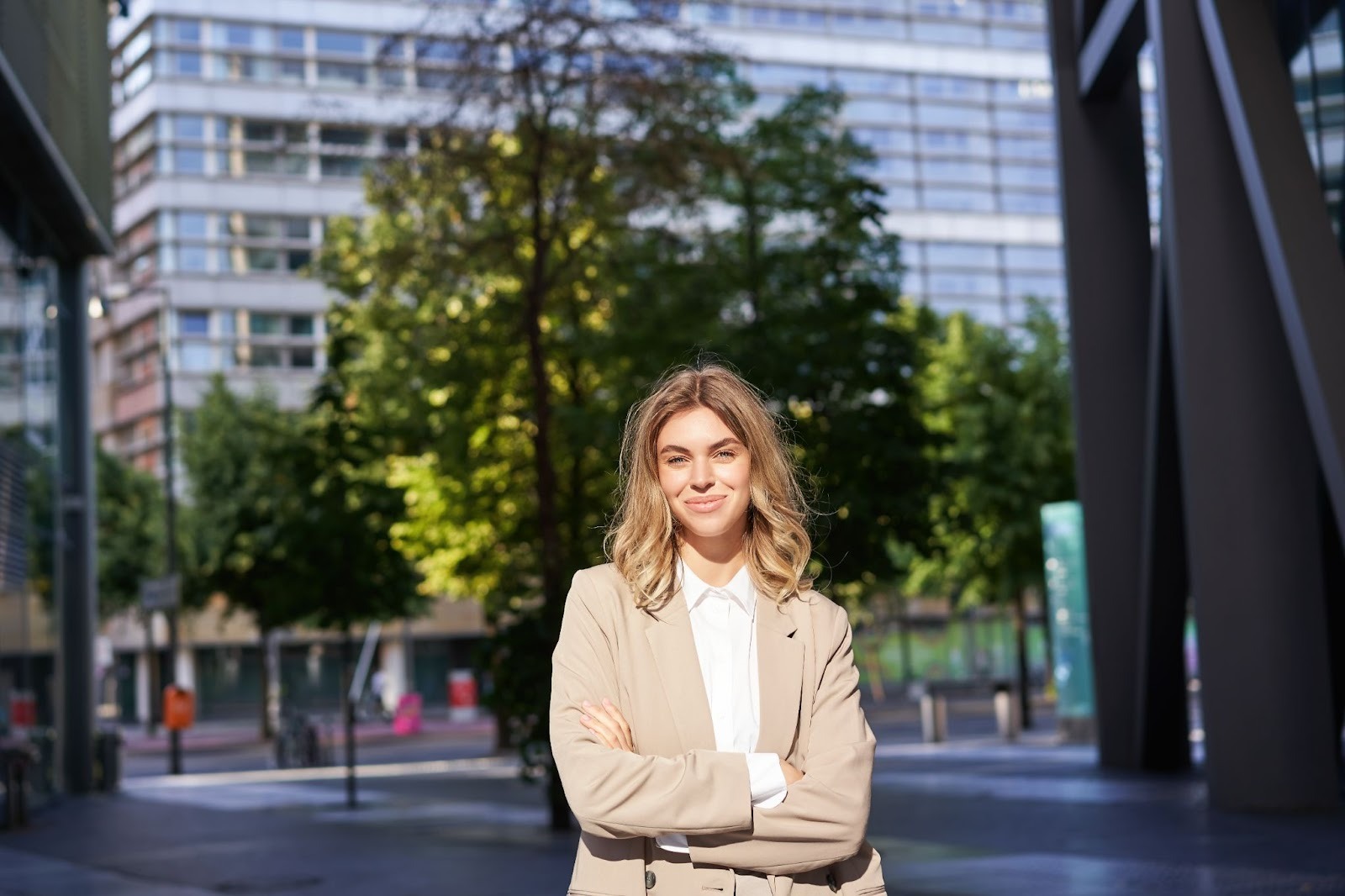 A blonde woman dressed up in business casual smiling in front of the camera while standing outside a building
