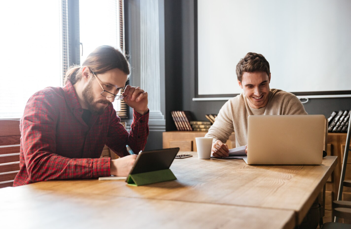 Two men sitting together at a table, using a laptop for the collaborative task of searching for the right addiction treatment center in South Carolina
