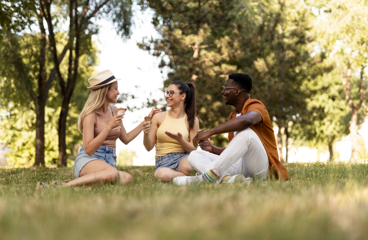 Three people sitting on the grass in a park, engaging in conversation and supporting each other even after rehab