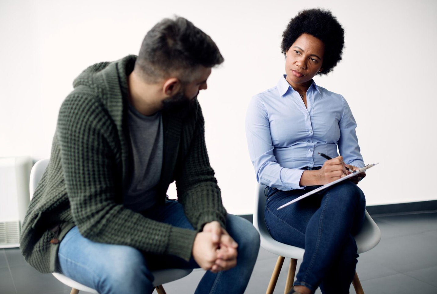 A clinician in a blue shirt taking notes while meeting with a client in a green sweater, illustrating individualized care during a PHP treatment session