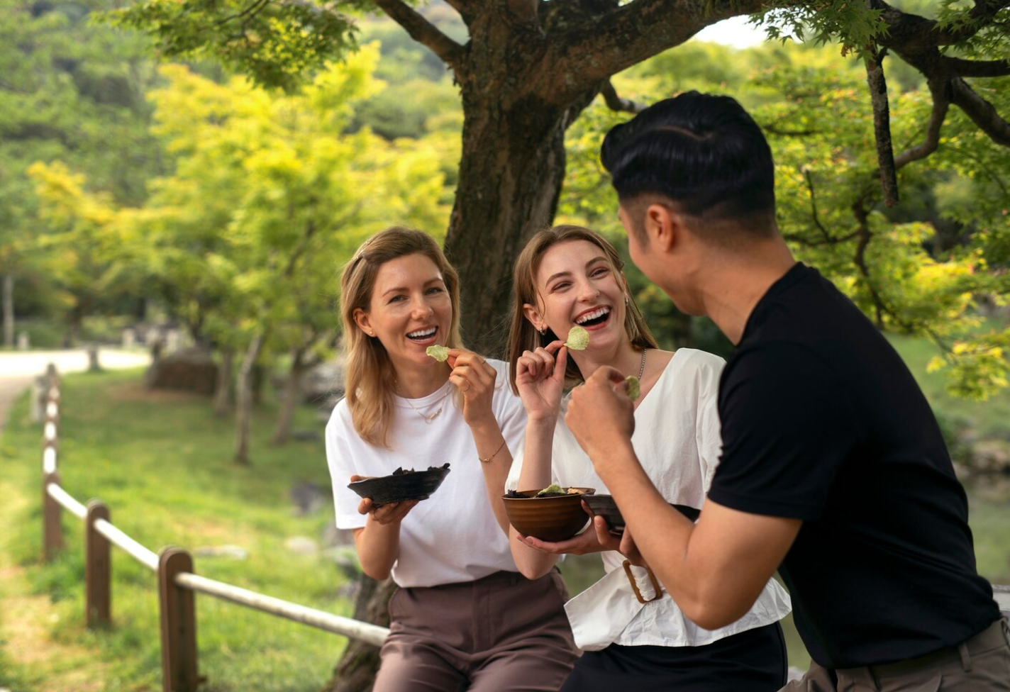 Three individuals sharing snacks and laughter in a green park setting, symbolizing balance, social support, and healing during PHP treatment
