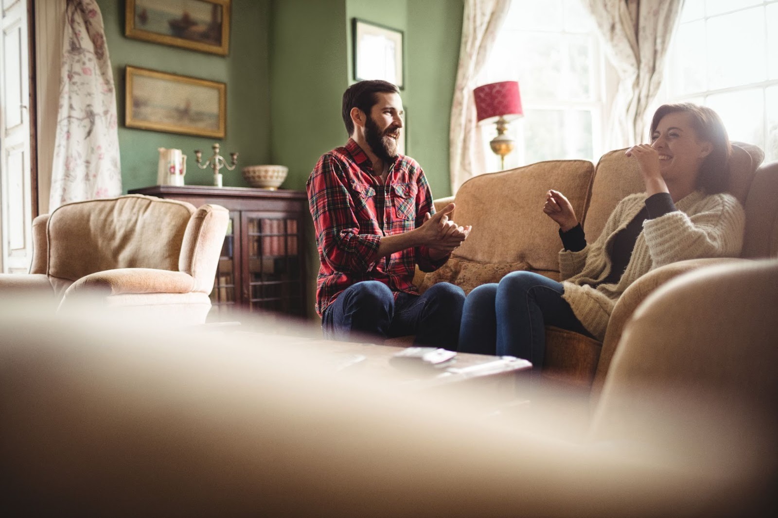 A man and woman sit laughing on a couch in a comfortable living room, reflecting connection and everyday stability often supported during outpatient addiction recovery