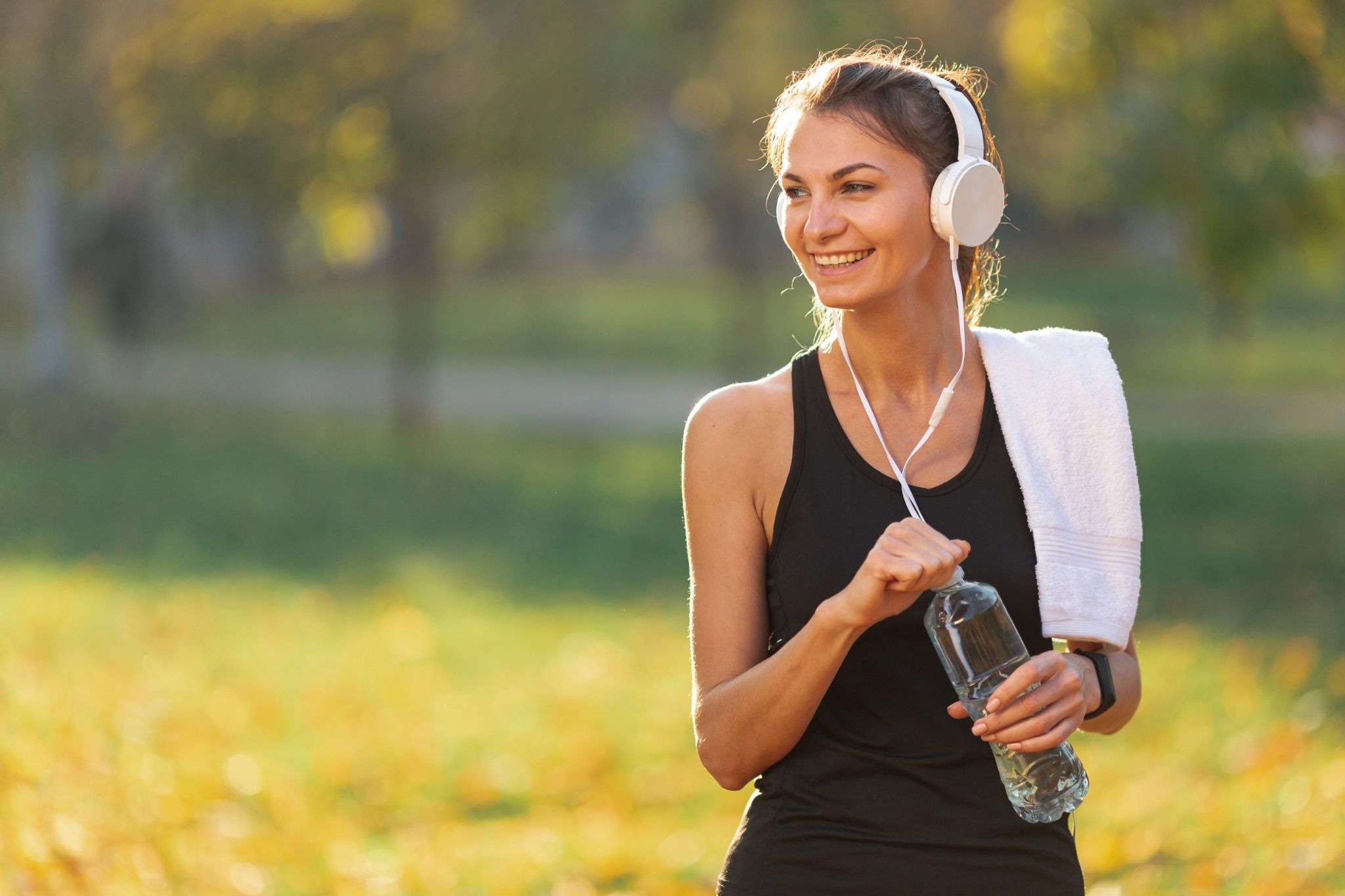 Woman outdoors after exercise holding a water bottle and listening to music, representing healthy habits during recovery